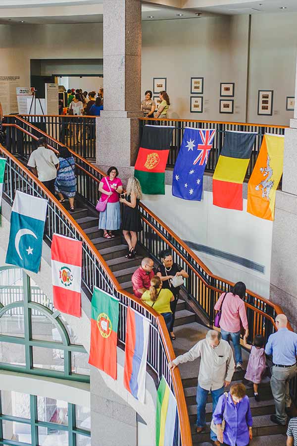 People walking down a grand staircase lined with many different countries' flags at the Bullock Museum
