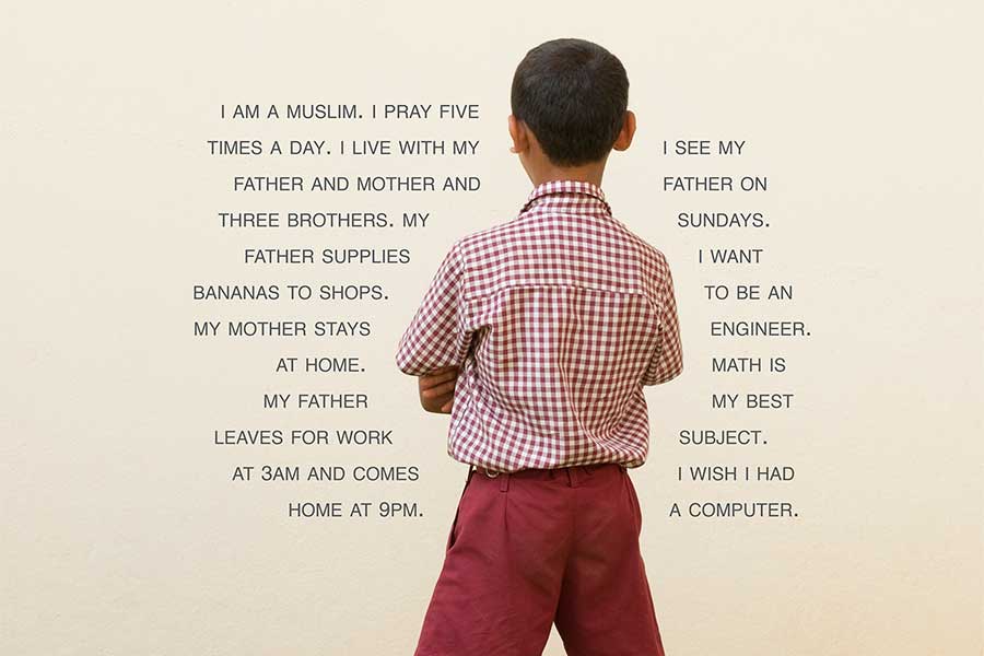 fourth grade student facing towards a blue and brick wall with white text on both sides of her