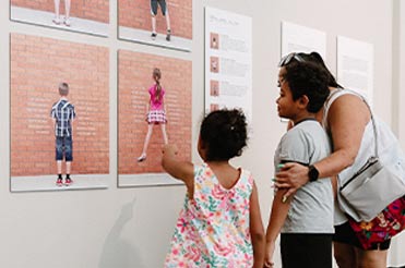 family of three standing in front of photographs in the exhibit "The Fourth Grade Project"
