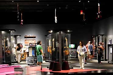 group of people in the Guitar exhibition at the Bullock Museum with many guitars in display cases