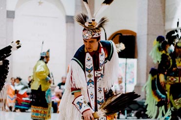 Man in traditional American Indian clothing holding a tambourine