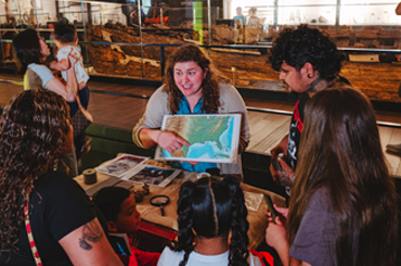 A person holding a map of the continental U.S. and presenting to a small group of museum visitors.