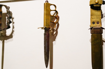 a trench knife with four finger slots as a handle hanging in a display case in the Bullock Museum