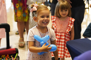 A child holding a blue animal balloon and smiling.