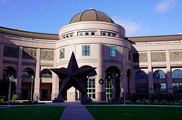 Exterior of Bullock Museum made of brown and red granite with a green dome and a large bronze star on the plaza