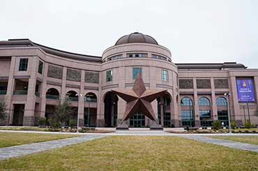 Exterior of Bullock Museum made of brown and red granite with a green dome and a large bronze star on the plaza