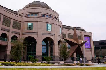 Exterior of Bullock Museum made of brown and red granite with a green dome and a large bronze star on the plaza