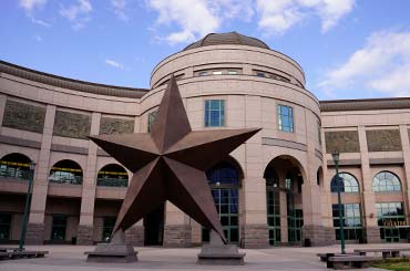 Exterior of Bullock Museum made of brown and red granite with a green dome and a large bronze star on the plaza