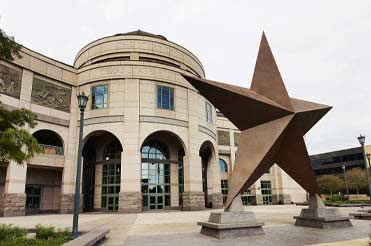 Exterior of Bullock Museum made of brown and red granite with a green dome and a large bronze star on the plaza