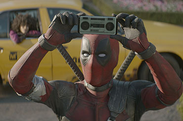 Still from Deadpool 2, Deadpool raises tiny boombox above head as a girl waits in a cab