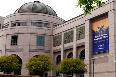 Side view of exterior of Bullock Museum made of brown and red granite with a green dome and a large bronze star in the plaza