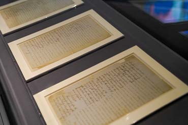three aged documents in a row under a display case