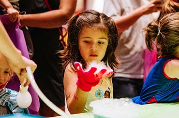 a young girl wearing a pink glove holding a piece of dry ice