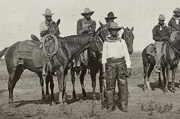 black and white photo of a group of African American cowboys, some on horses, some standing with rope