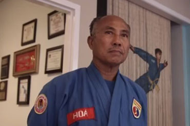 Closeup of a man, Master Hoa, wearing a blue martial arts uniform looking above the camera
