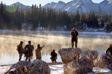Group of people in winter native clothing looking towards a mountain and a lake