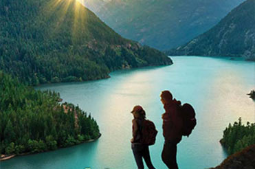 two people looking out over a mountain and a lake with the sun setting