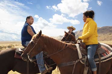 Three people on brown horses in a landscape with a mountain and blue skies