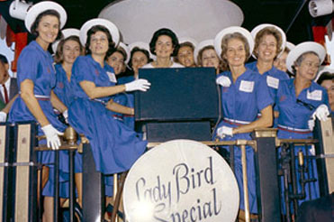 Ladybird Johnson and a group of women on a stage with a sign in front that reads, Lady Bird Special
