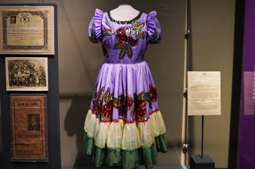 A dress with purple, yellow, and green layers and many sequins on a mannequin in a display case.