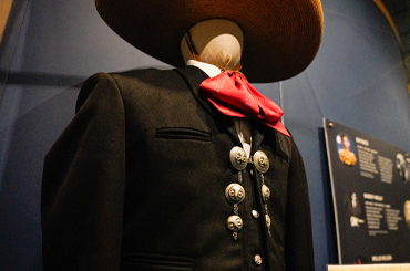 A black mariachi suit with a red bow, on a mannequin in a museum display case.