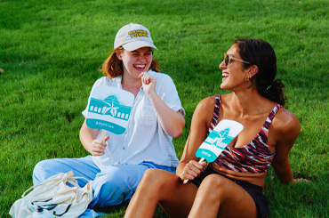 two women sitting outside waving paper fans and watching a live music performance on the Capitol Mall outside the Bullock Museum.