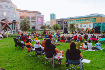 people sitting on lawn chairs watching a live music performance on the Capitol Mall outside the Bullock Museum.