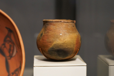 an aged brown clay pot in a museum display case.
