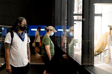 two people wearing masks looking at a large display case full of objects from a ship in the Bullock Museum