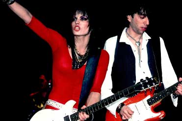 Joan Jett and her guitarist holding guitars, Jett's arm is raised in the air