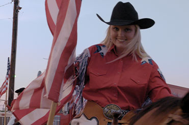 woman in a red shirt and black cowboy hat sitting on a horse with an American flag