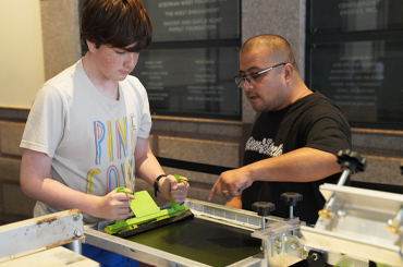 An adolescent doing a screen printing craft with an instructor.