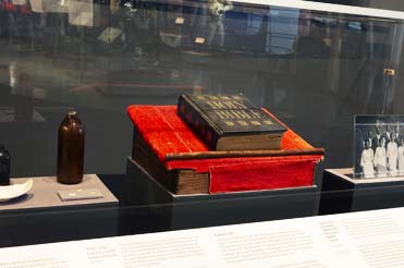 a bible, red lectern, a brown bottle, and a black and white photograph in a display case in the Bullock Museum Texas Story Project exhibition