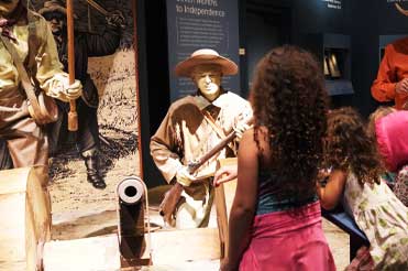 two children standing in front of a replica of soldiers holding guns and standing around a canon in the Texas Revolution