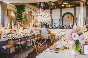 long white tables lined with golden colored chairs and set with fine dining dishes and pink center floral pieces in the Bullock Museum Grand Lobby