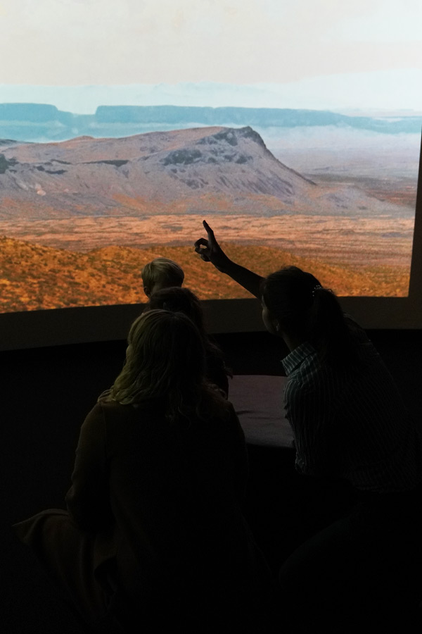 a group of people pointing to a large screen displaying Texas desert landscapes.