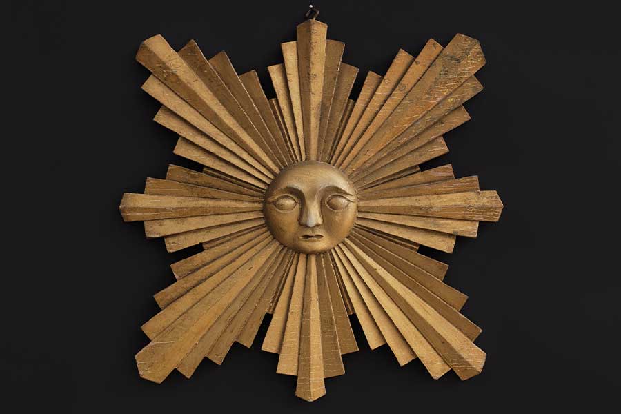gold colored, wooden sun with extreme extruding rays on a black background