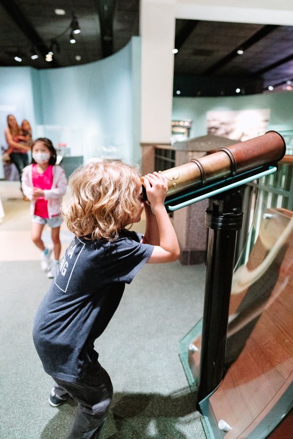 young child looking through gold and wooden spyglass